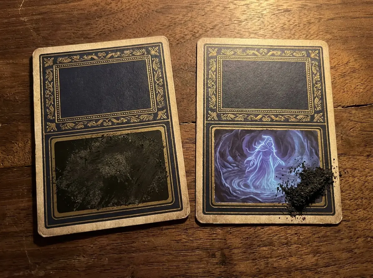 Two MORANA cards: one still sealed under ash, one scratched open to its Nav face, with ash residue beside it